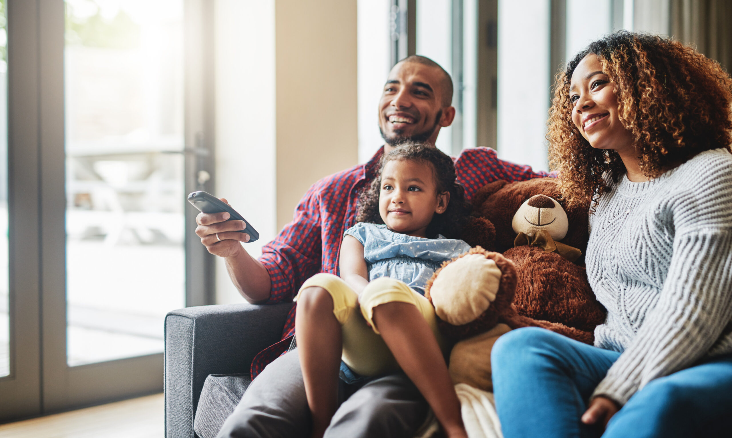 Love, smile and family on a couch, watching tv and bonding on a weekend break, home or chilling. Happy parents, mother or father with kid, female child or daughter on a sofa, happiness and television.